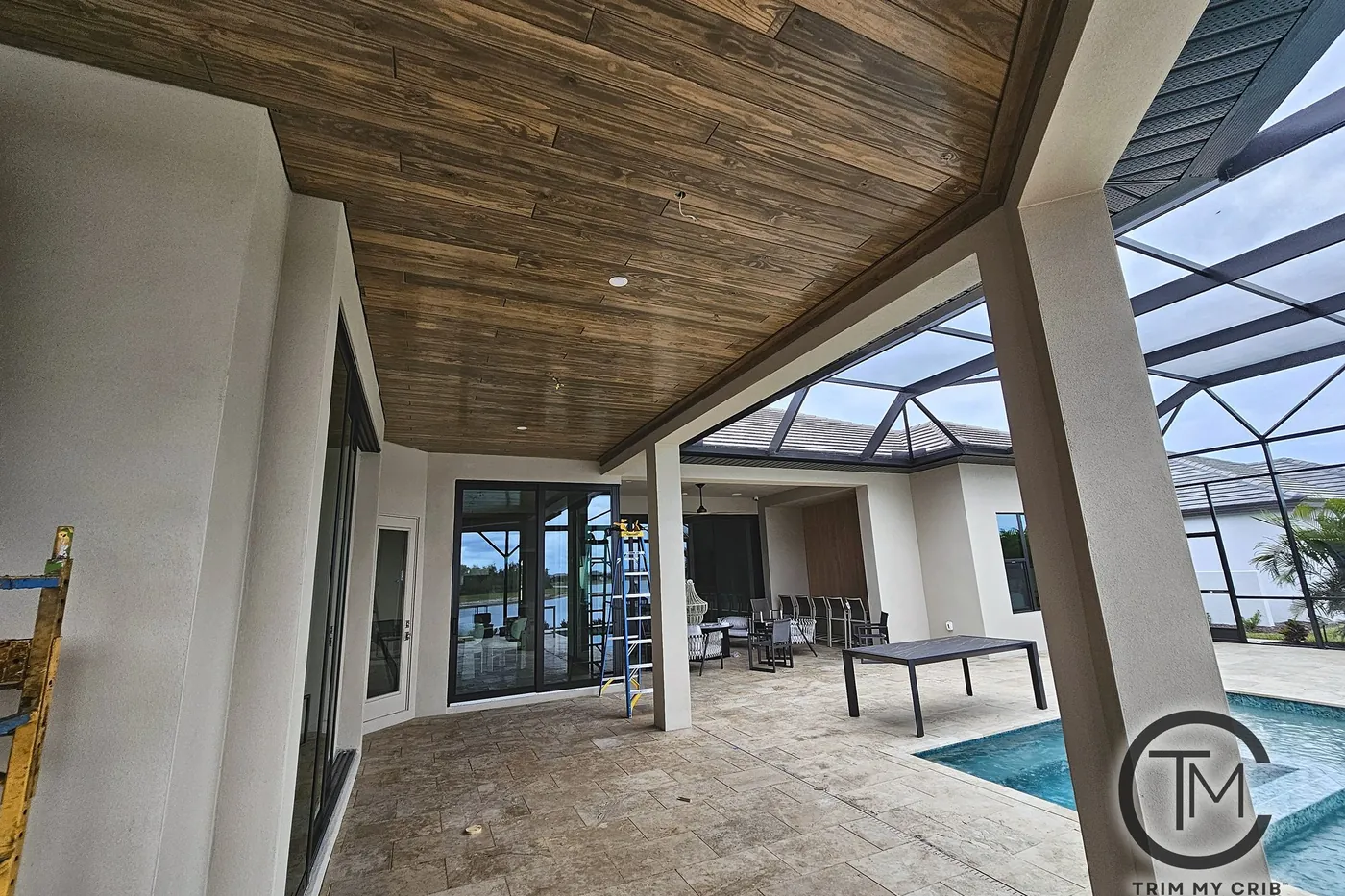 Covered poolside patio with a stained wood ceiling over a wide paver floor and a table by the pool