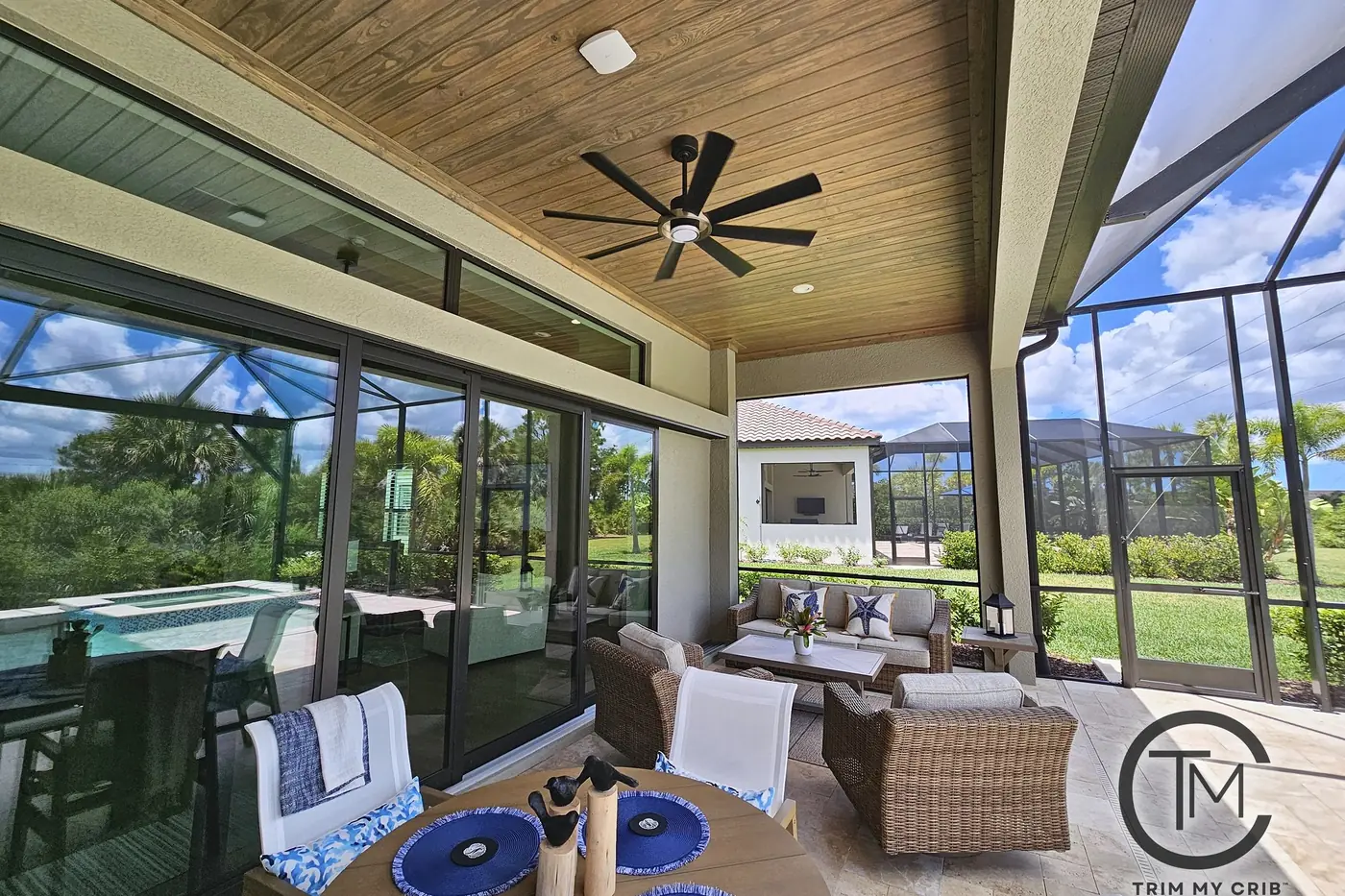 Lanai dining table under a light stained wood ceiling with a large ceiling fan and a view across the pool cage