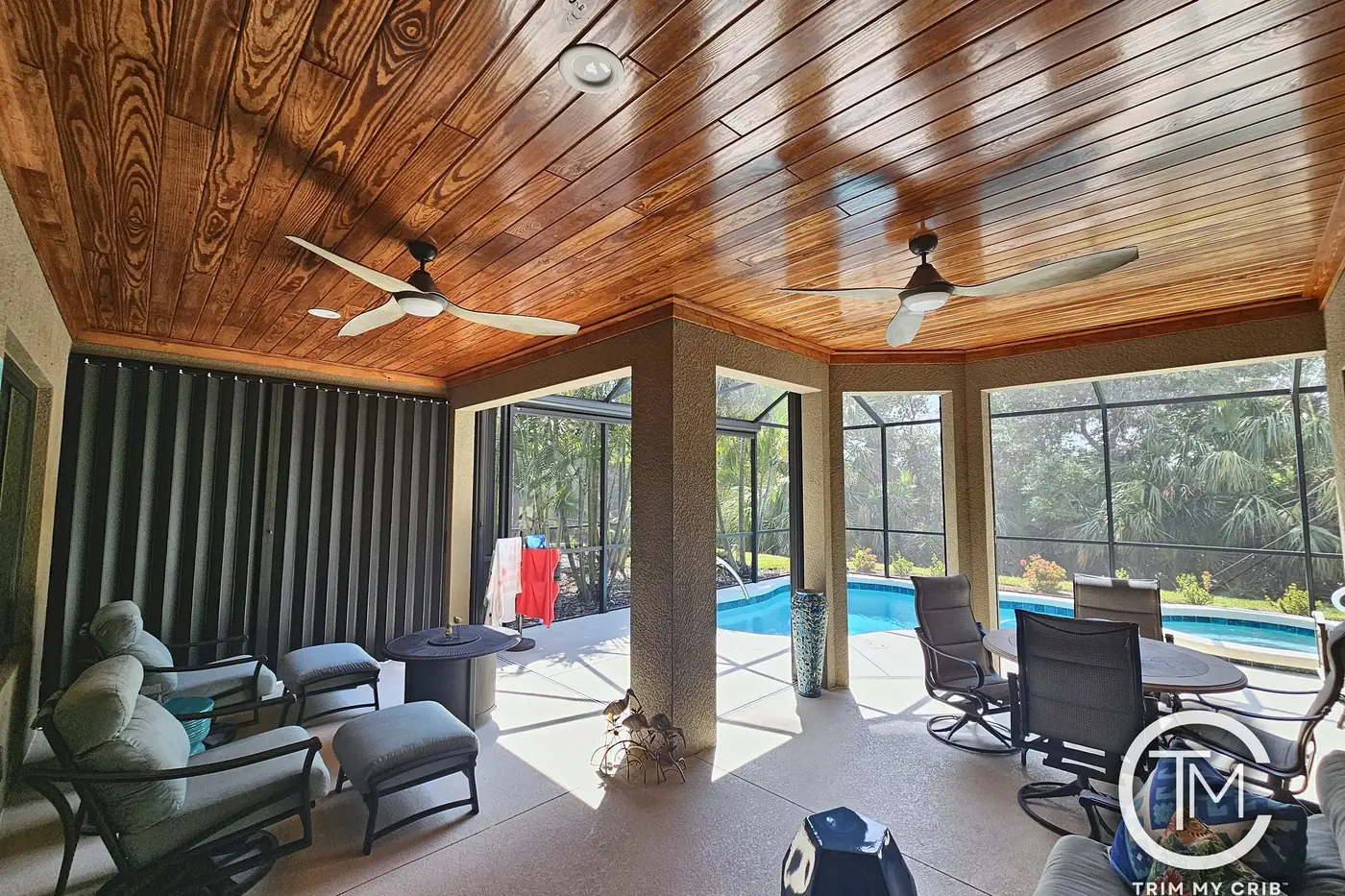Screened lanai with a golden stained wood ceiling, two ceiling fans and outdoor seating beside the pool
